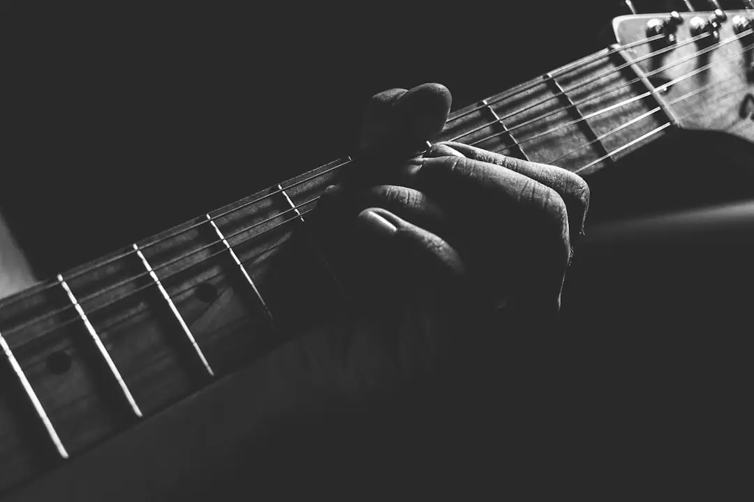 A monochromatic bend in a fender stratocaster by Guitar Brands grayscale photo of person holding guitar neck and strings