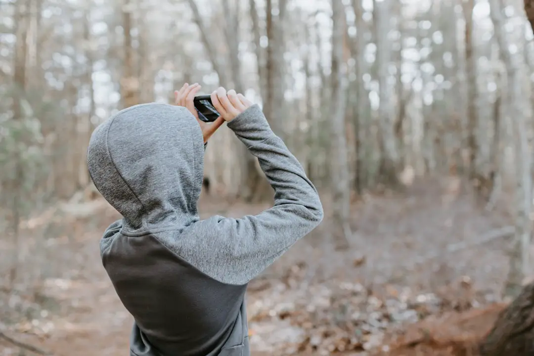 Boy taking photos in the woods with camera phone by Guitar Brands man in gray sweater holding black camera